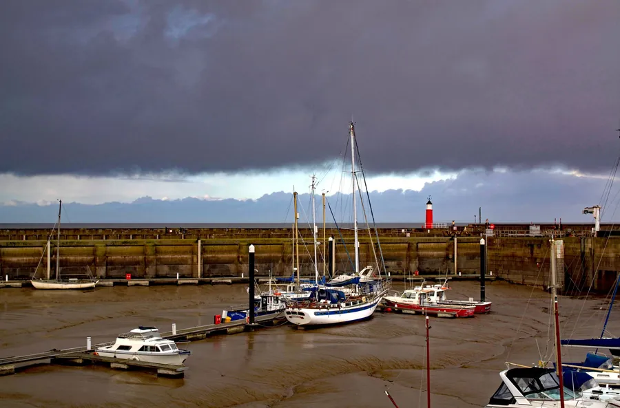 A Somerset harbour on the Bristol Channel under storm cloud, showing the coastal exposure affecting Weston-super-Mare roofs
