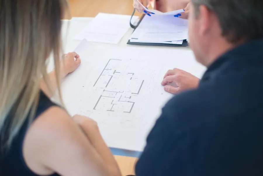 Two people going over a printed floor plan and paperwork at a desk, checking building control details for a flat roof in Burnham-on-Sea
