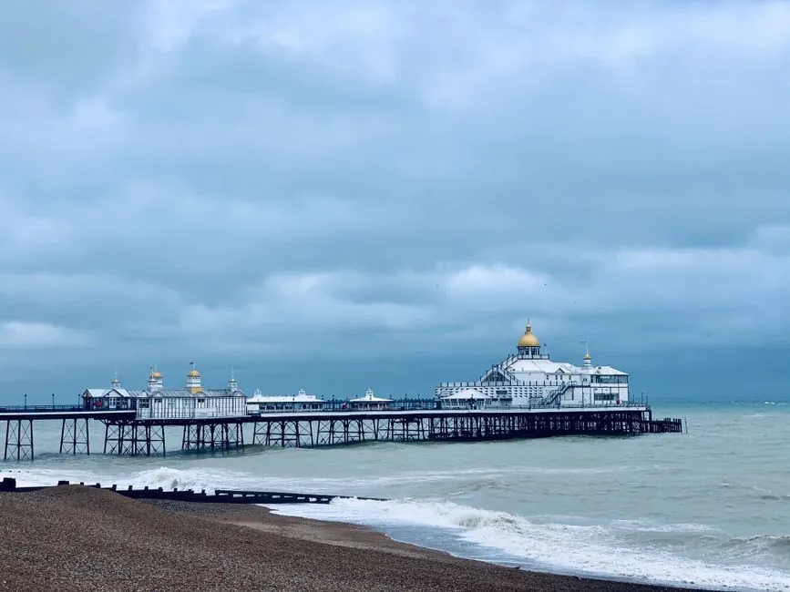 A British seaside pier under heavy grey cloud, the exposed coastal conditions that drive flat roof wind uplift design near Weston-super-Mare