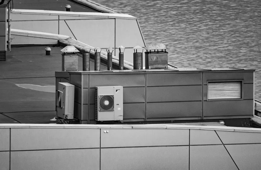 Black and white view of a commercial flat roof with air conditioning units, vent stacks and a plant enclosure, the kind of roof found over shops and units in Portishead and Nailsea