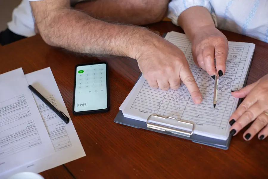 Two people going through handwritten figures on a clipboard beside a phone calculator, comparing written flat roof quotes for a Clevedon property