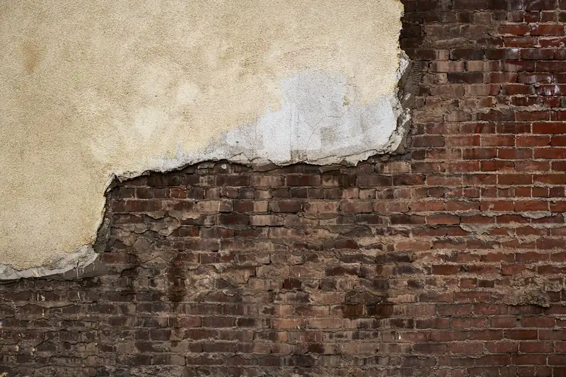 Render that has blown and fallen away from an exterior brick wall, the sort of surface a flat roof flashing is often dressed over in Weston-super-Mare