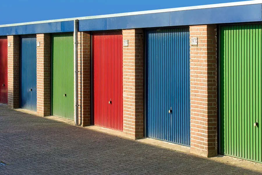 A row of brick lock-up garages with coloured up-and-over doors under a continuous flat roof edge, typical of estate garage blocks around Nailsea