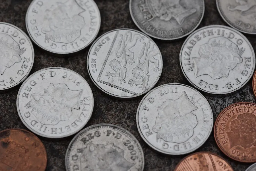 British ten pence and penny coins spread across a stone surface, illustrating the cost of a flat roof abutment repair against a full re-cover in Weston-super-Mare