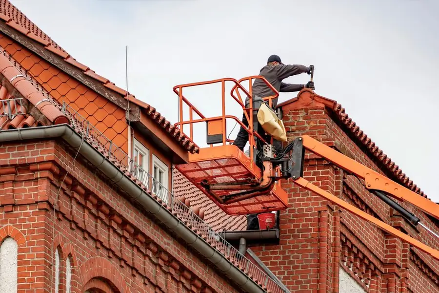 A roofer inspecting the condition of a roof on a brick building before advising on repair or replacement