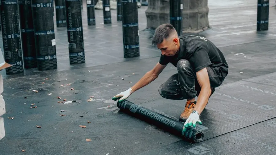 A roofer bonding new waterproofing material over a section of flat roof during a localised repair