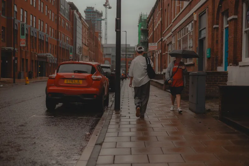 A rain-soaked British street with pedestrians under umbrellas and wet brick buildings, the weather that separates a genuine abutment leak from condensation