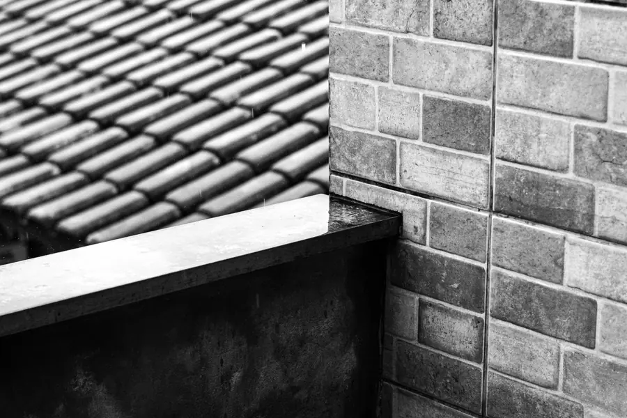 Rain falling where a tiled roof slope meets a brick wall and coping, the kind of abutment where dormer roofs in Weston-super-Mare let water in