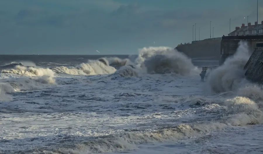 Waves breaking over a seawall under grey cloud, the kind of onshore weather that drives rain into dormer roofs in Weston-super-Mare