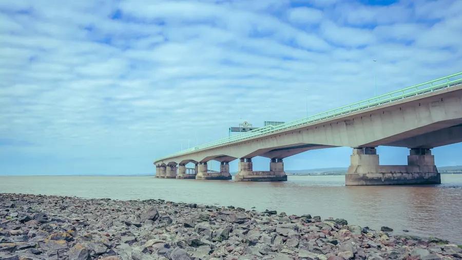 The Prince of Wales Bridge crossing the wide, muddy Severn estuary from a stony foreshore, the stretch of water upstream of Portishead