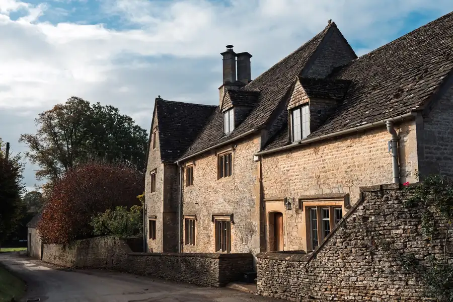 Stone slate roof slopes running into solid stone gable walls on an old English house, the kind of abutment junctions that fail before the roof covering does