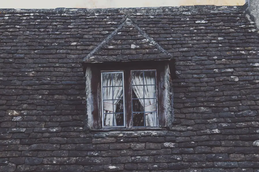 A small dormer window set into an old slate roof, the kind of compact roof where repair or full re-covering is decided