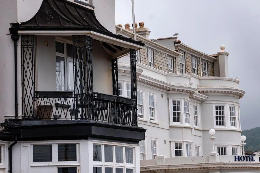 White-painted Victorian seafront buildings with a canopied bay and iron balcony, the type of frontage whose small flat roofs need care in Burnham-on-Sea