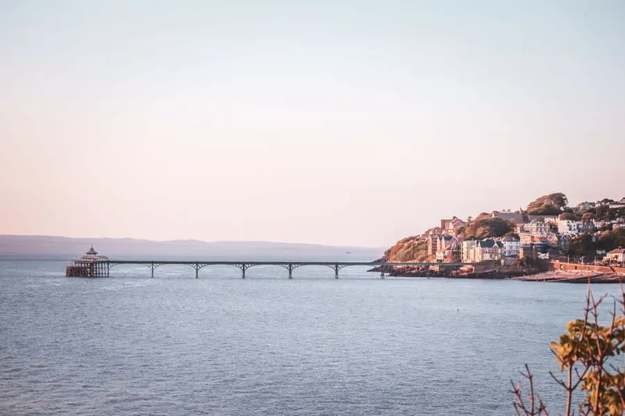 Clevedon's Victorian pier stretching out over still water at dusk, with the wooded headland behind it